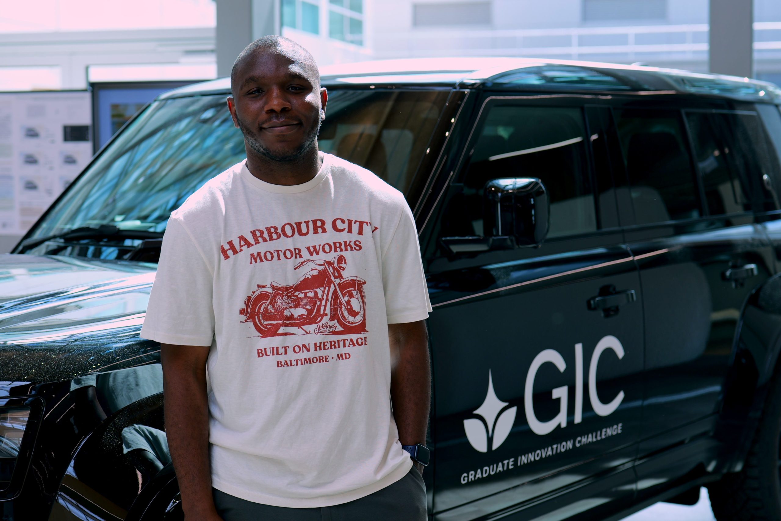 Emmanuel Okpaluba beside a Graduate Innovation Challenge branded vehicle